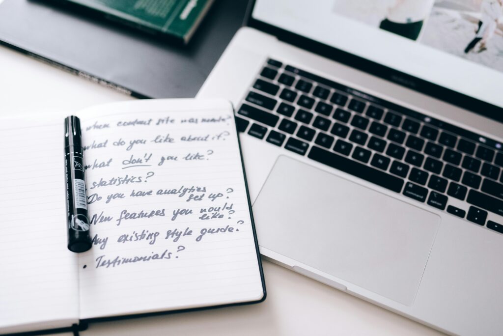 pexels-photo-7818111-7818111 A notebook with handwritten notes next to a laptop on a workspace desk.